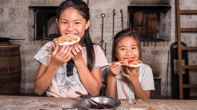 Des visiteurs prennent une bouchée de pain bannock frais dans la boulangerie. Lieu historique national de Lower Fort Garry.