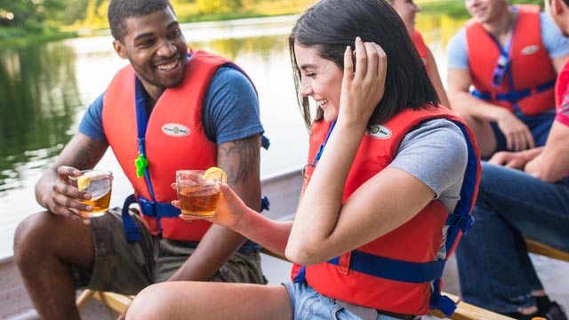 Visiteurs à bord d'un canot voyageur de 10 places savourant un verre de thé glacé par un après-midi ensoleillé dans le cadre de l'excursion à la pagaie Balade sur la Mersey.