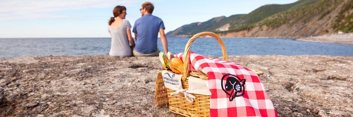 Un couple apprécie le superbe panorama de son coin de pique-nique parfait à La Bloc, où il dégustera son pique-nique commandé à un restaurant local, livré dans un panier de l’île du Cap-Breton et accompagné d’une couverture de pique-nique de Parcs Canada, au parc national des Hautes-Terres-du-Cap-Breton. 