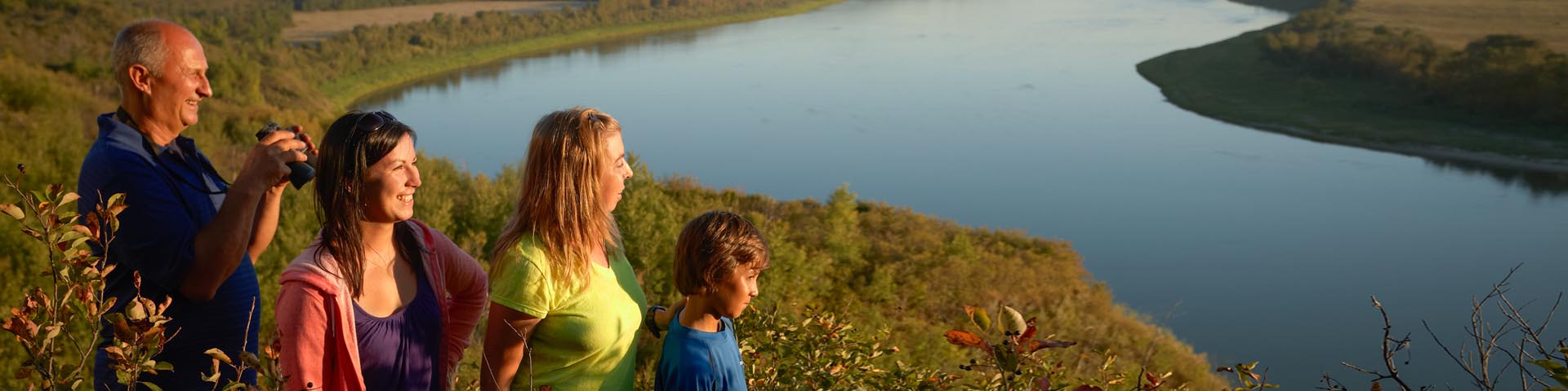 Quatre visiteurs regardent le paysage au coucher du soleil près de la rivière au lieu historique national de Batoche.