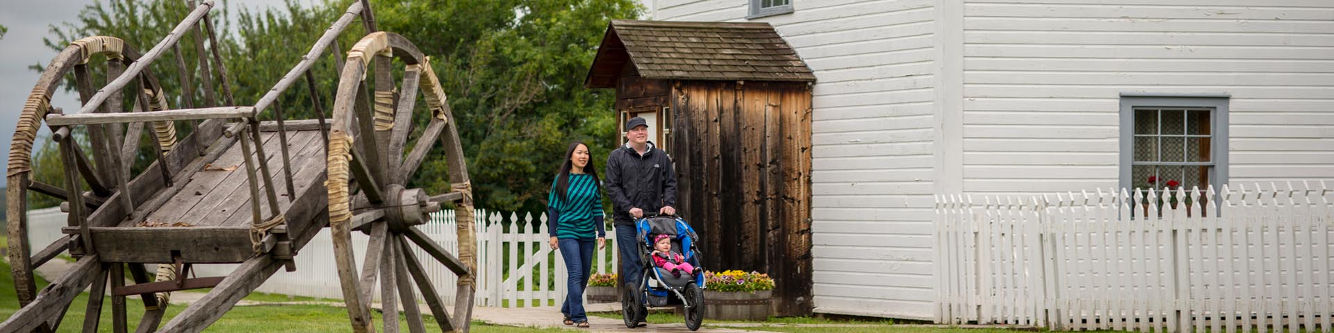 Deux adultes avec un enfant dans une poussette marchent le long de la promenade près de l'église et du presbytère au lieu historique national de Batoche.