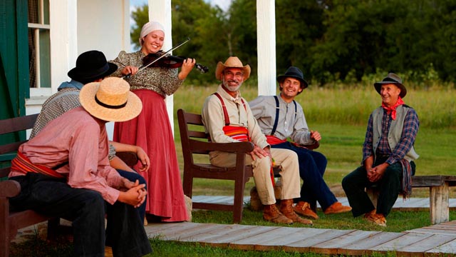 A costumed interpreter playing the violin on a terrace among other interpreters at Batoche National Historic Site.