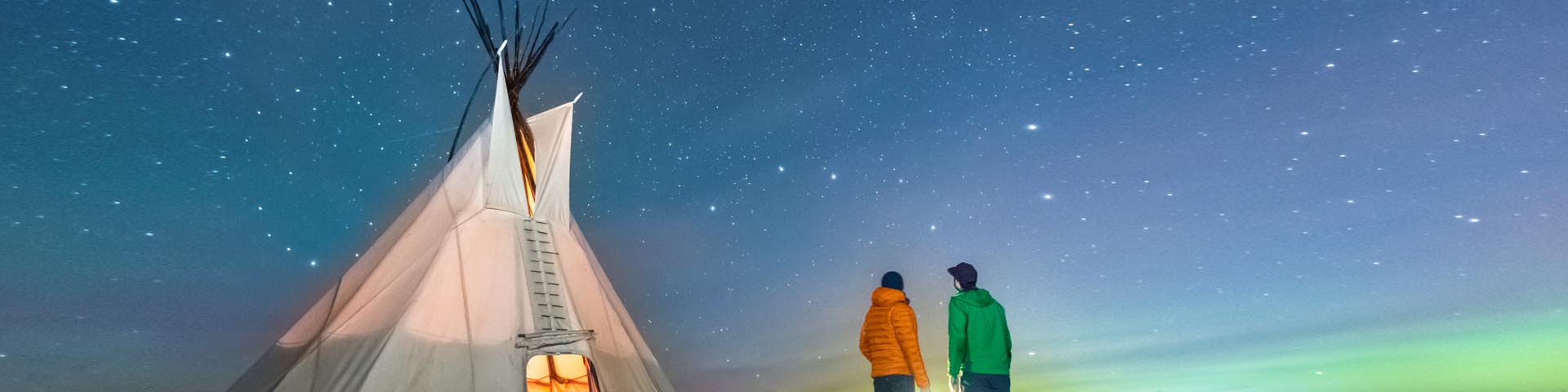 Two visitors gazing at the Big Dipper stars outside a tipi on a starry night at Rocky Mountain House National Historic Site.