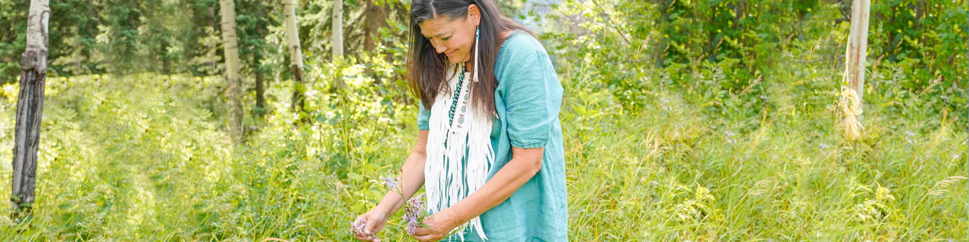 An Indigenous woman picks plants in the forest of Jasper National Park.