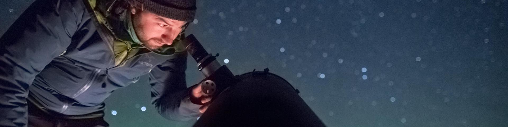 	Un visiteur observe le ciel étoilé à l'aide d'un télescope astronomique et s'émerveille devant la brillance des étoiles et la chorégraphie des aurores boréales dans la réserve de ciel étoilé