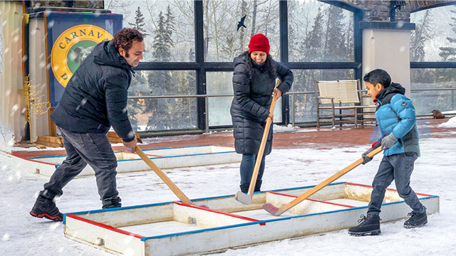 Family playing hockey, moving the puck inside a wood box arena.