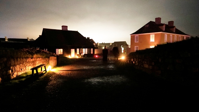 Deux des bâtiments historiques de la forteresse de Louisbourg sont éclairés par des lampes dans une ambiance inquiétante.