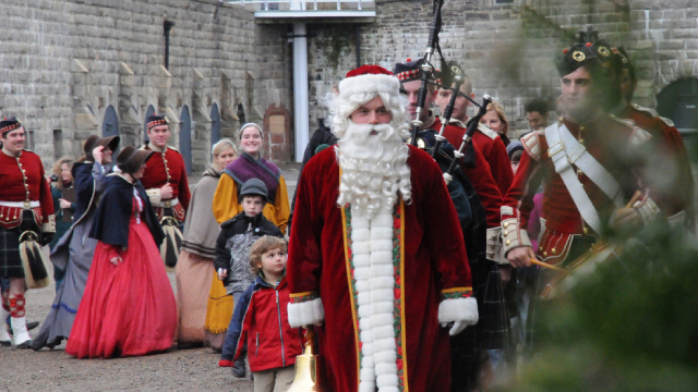 Historic interpreters in costumes stand behind a man dressed in a Santa costume in the citadel.