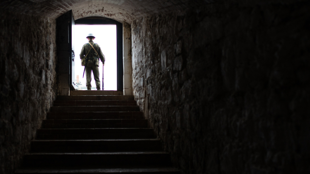 A man in a soldier uniform stands at the end of a dimly lit tunnel.