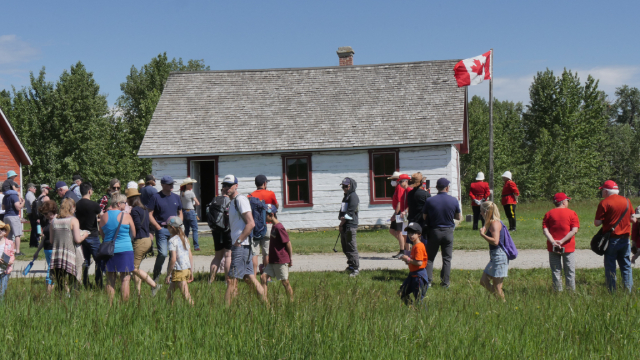 Des visiteurs rassemblés devant un bâtiment historique pour la fête du Canada.