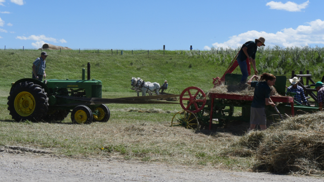 Des gens travaillant avec un tracteur et différents équiments de ferme dans un champs lors d'une journée ensoleillée.