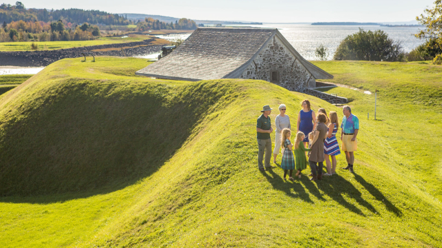 Visitors standing on earthen wall at Fort Anne, overlooking the powder magazine, fall trees and the Annapolis River.