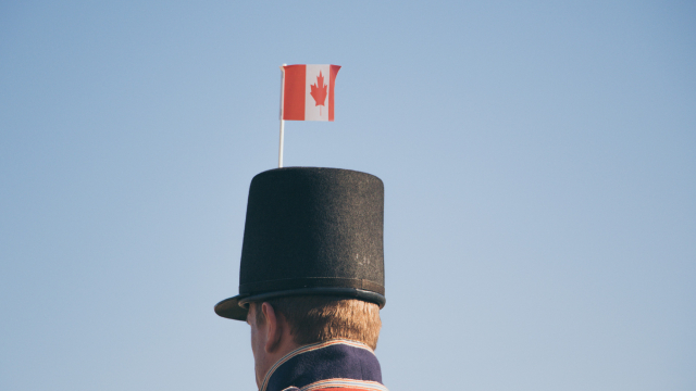 L'arrière de la tête d'un soldat en costume, avec un petit drapeau du Canada sur le dessus de son chapeau.