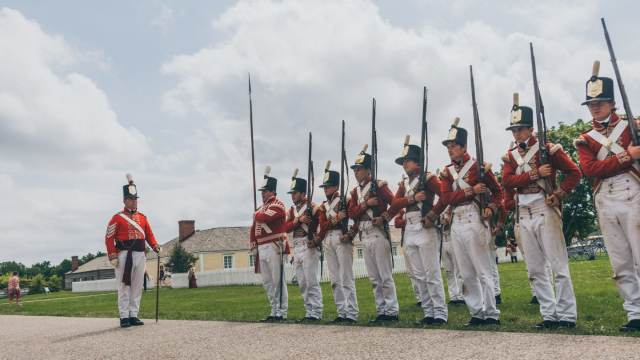 Un groupe de soldats en costume avec des répliques de fusils devant un fort historique.