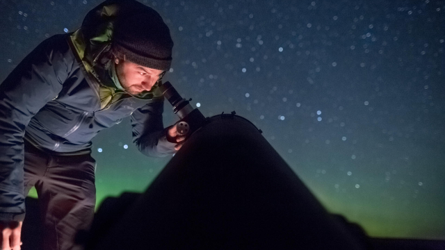 A man looks into a telescope on a starry eveneing. 