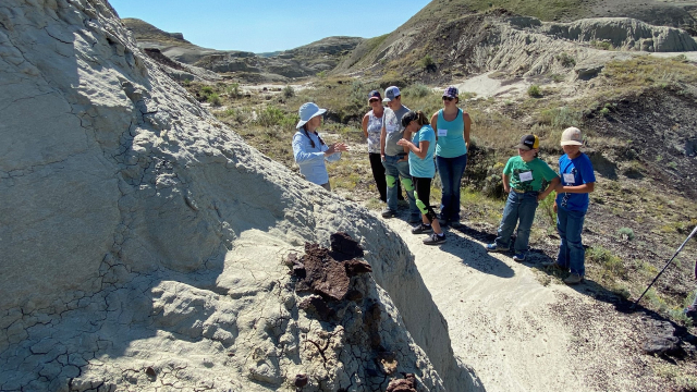 Des visiteurs font une randonnée sur de gros rochers avec des collines de prairie en arrière-plan.