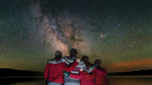 Four visitors in matching red jackets gaze at the Milky Way. 