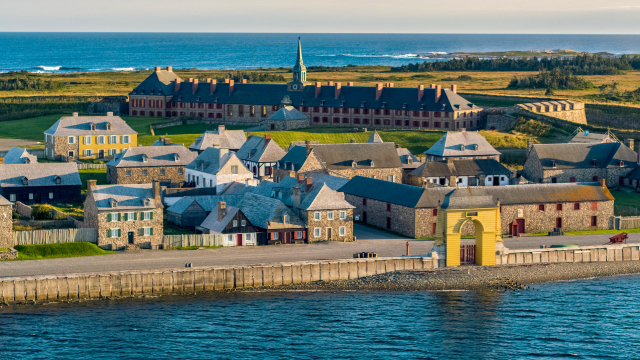 An aerial view of the entire set of buildings of The Fortress of Louisbourg on a sunny day with bright blue waters. 
