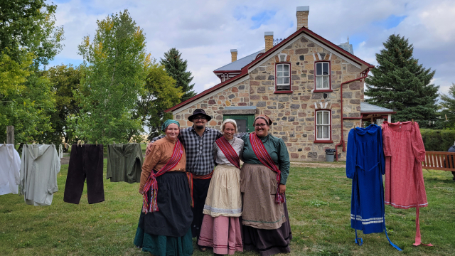 Parks Canada interpreters in traditional Métis clothing with a historic building in the background. 
