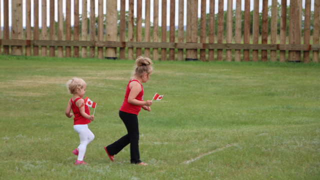 Alt text: Deux enfants courent dans un champ, des drapeaux canadiens à la main.