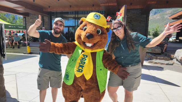 Deux employés de Parcs Canada sourient à la caméra avec Parka le castor, la mascotte de Parcs Canada.