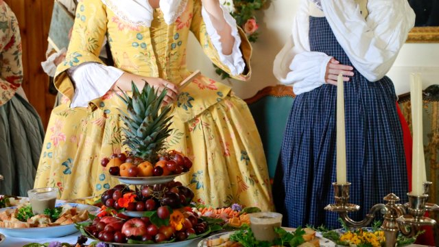 Une table garnie d’un festin, avec des guides en costume d’époque à l'arrière-plan.