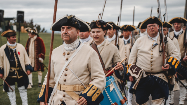 Des acteurs de reconstitution en uniforme de soldat défilent au son du tambour.