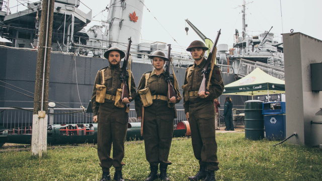Trois soldats en uniforme posent devant le destroyer de classe Tribal.