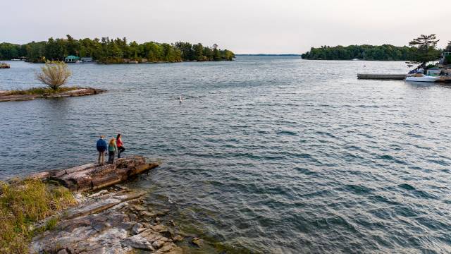 Trois visiteurs sur un rocher au bord du fleuve Saint-Laurent par une journée d'été nuageuse.