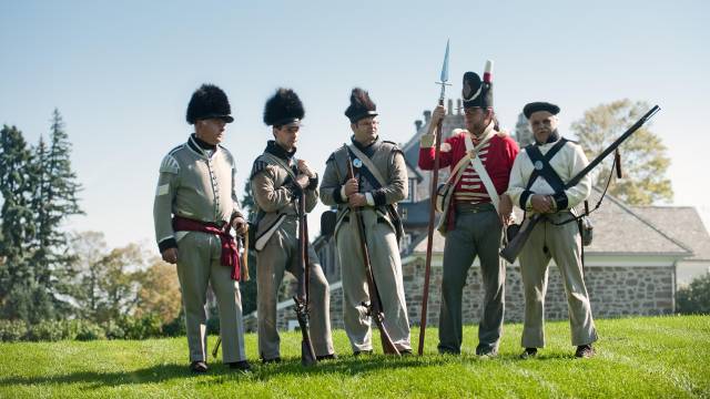 Un groupe de reconstituteurs en costumes du 18e siècle pose pour une photo devant un fort historique.