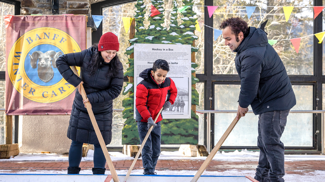 Une famille de trois joue au hockey en boîte lors du Carnaval de Banff.