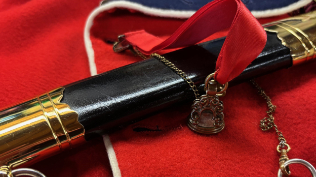 A close-up of a historic sword laying on a red uniform. 