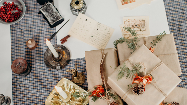 Quatre cadeaux emballés avec des matériaux recyclables sont disposés sur une table avec des chandelles, des canneberges, de l’encre et d’autres objets festifs