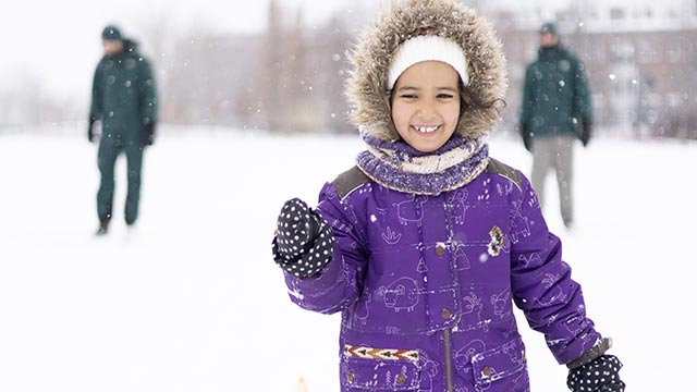 A young girl in a winter urban landscape with two Parks Canada staff members in the background.