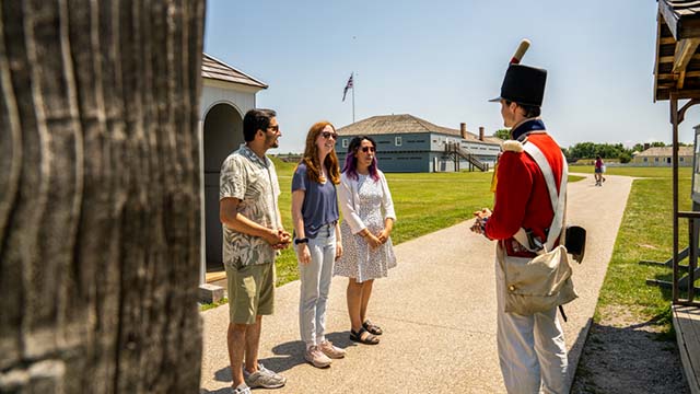 A group of 3 stands in front of a costumed staff member dressed in a historic soldiers uniform.