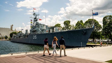 Three visitors walk towards a grey warship.