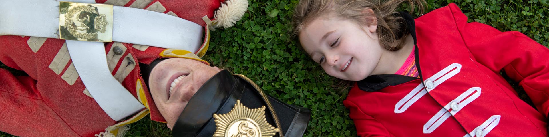 A girl dressed as a soldier and a soldier lie on the grass at Fort Malden National Historic Site.