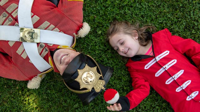 A girl dressed as a soldier and a soldier lie on the grass at Fort Malden National Historic Site.