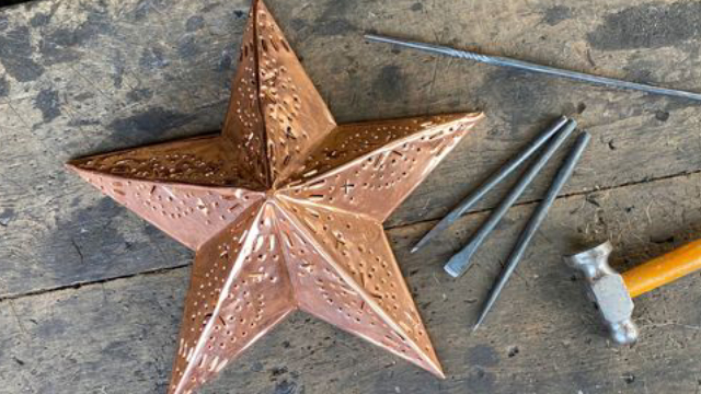 A copper star on a wooden table with 3 nails and a hammer.