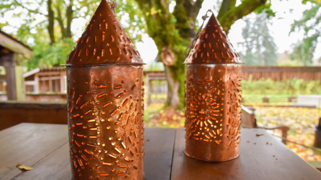 Two copper lanterns on a wooden table with a tree in the background.