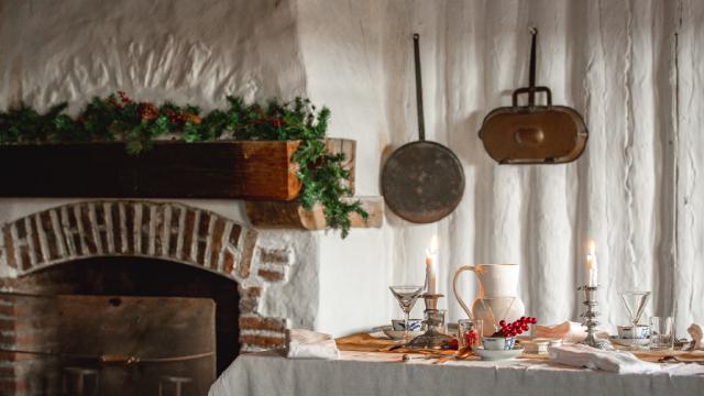 A table set with candles, cutlery and various items in front of a festively decorated fireplace with garland on it.