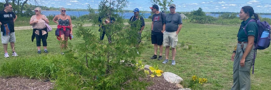 Visitors stand around the medicine garden with a Parks Canada staff member on a sunny summer day.