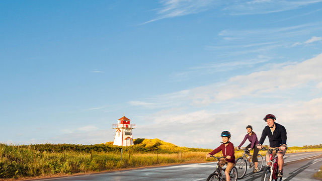 Trois cyclistes sur la route près d'un phare.