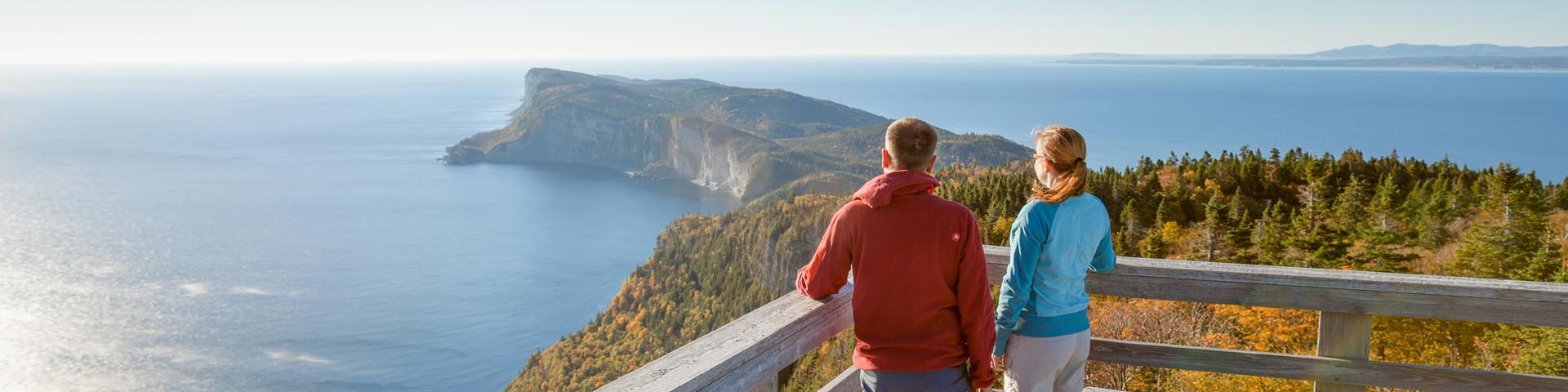 Deux jeunes adultes sont en haut de la tour d'observation du mont St-Alban, à 283 mètres d’altitude et regardent le paysage de mer, de forêt et de falaises au parc national Forillon.