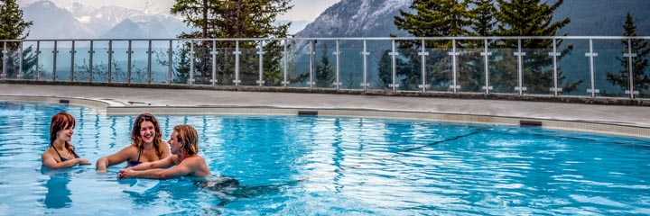Three people chatting in the pool with a mountain backdrop at Upper Banff Hot Springs.