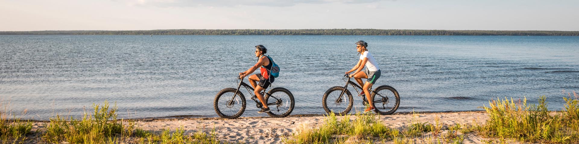 Visitors ride fat bikes along the beach on South Shore Trail. Riding Mountain National Park.