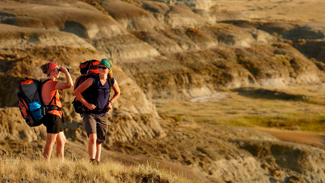 Two women with backpacks in the badlands of the Valley of 1000 Devils in Grasslands National Park.