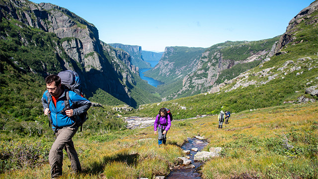 Four hikers ascend the Long Range plateau, with the Western Brook Pond fjord in the background at Gros Morne.