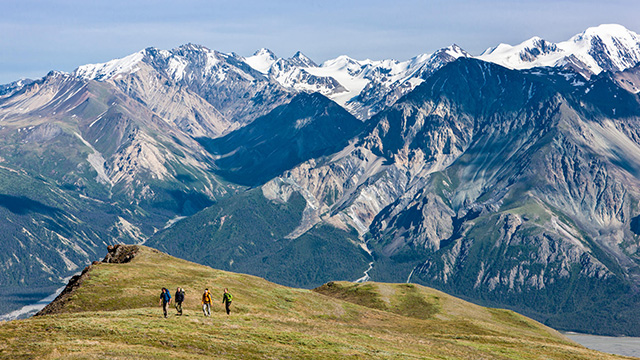 Four hikers in the Ä’äy Chù Valley, with mountains in the background at Kluane.