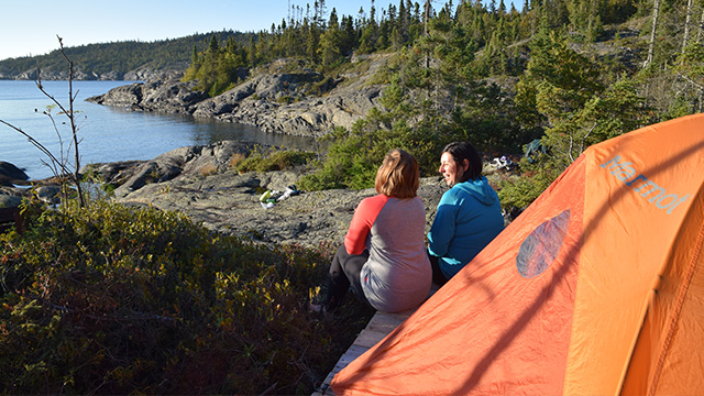 Two women beside their tent along the Coastal Hiking Trail, with Lake Superior in the background at Pukaskwa.